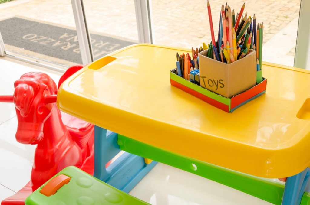 Fotografia de uma mesa de atividades infantil, com base amarela. Em cima da mesa lapis de cor e giz de cera.